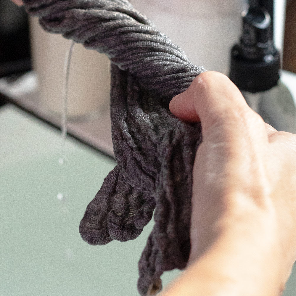 wet double gauze linen face wash cloth being rung out over a sink