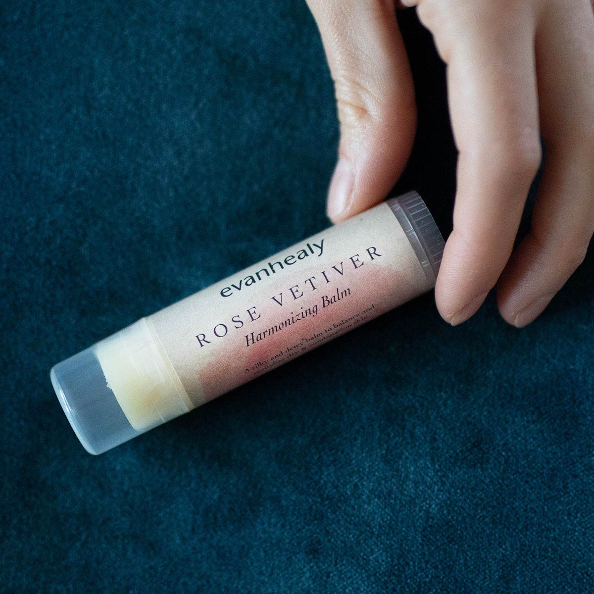 moisturizing rose vetiver stick balm in fingertips with blue background