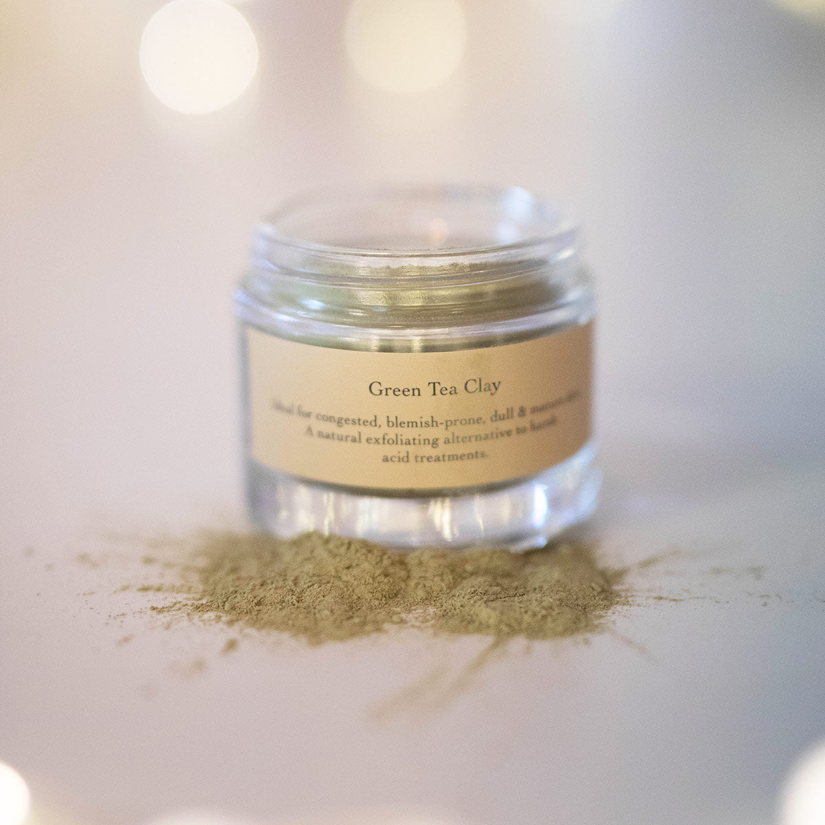 green tea clay mask in glass jar with lid off spilled on surface to show texture