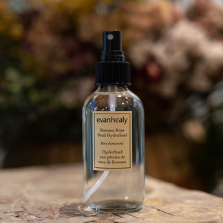 Front view of Sonoma Rose Petal HydroSoul spray bottle with label and black pump against blurred floral background
