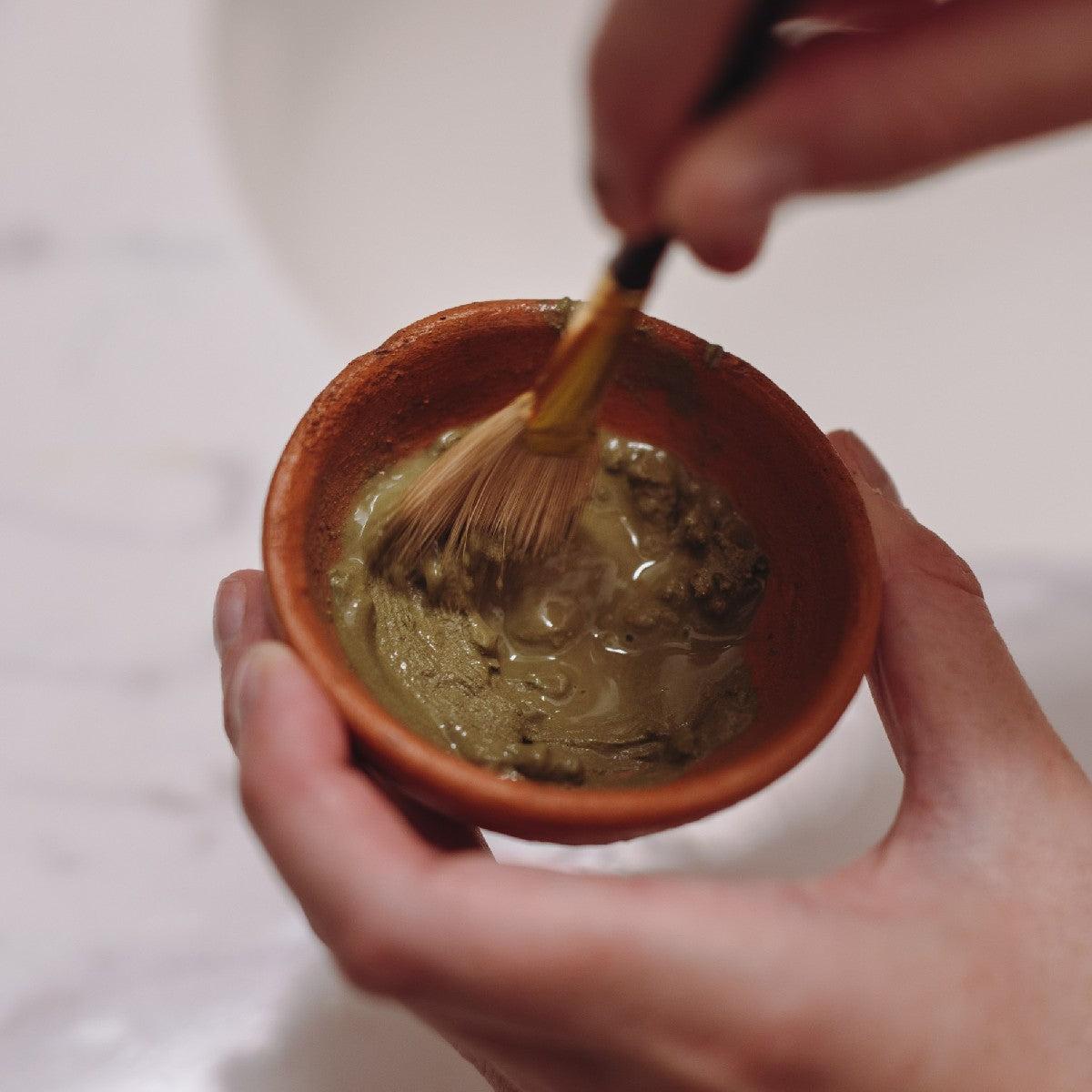 evanhealy green tea clay mask mixed with fan brush in terra cotta bowl on bathroom counter
