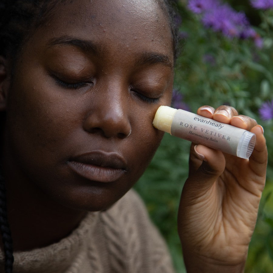 model applying rose vetiver moisture balm stick to face in nature
