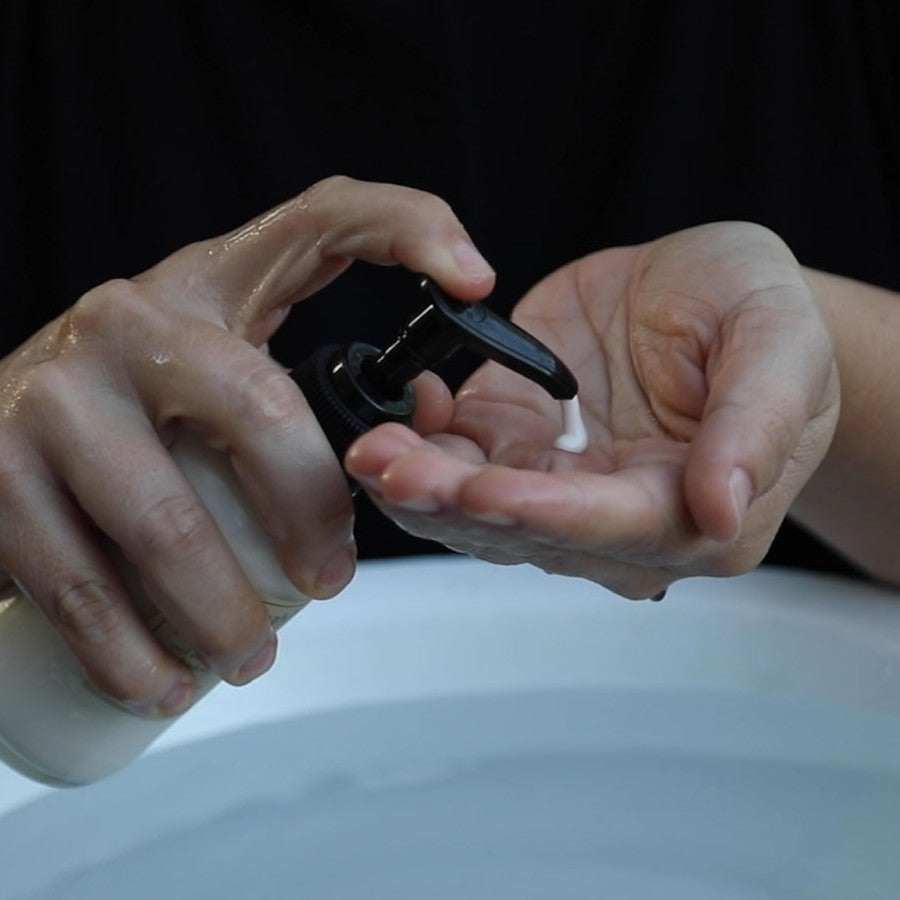 simply basic cleansing milk facial cleanser pump texture in palm of hand over sink full of water