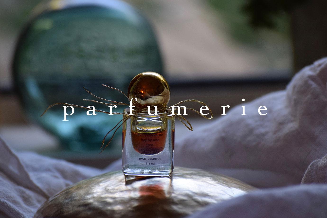 Front view of glass perfume bottle with gold cap, amber liquid on draped fabric and blurred vase, overlaid text parfumerie