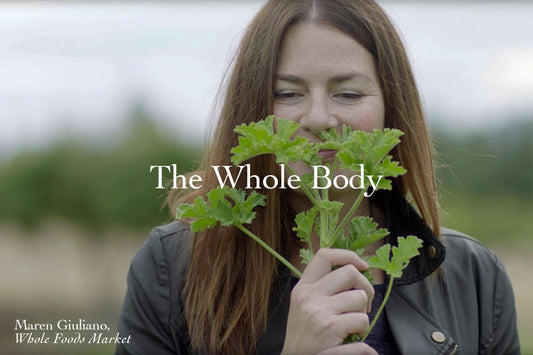 Woman holding and smelling a sprig of green herb outdoors with overlaid headline The Whole Body