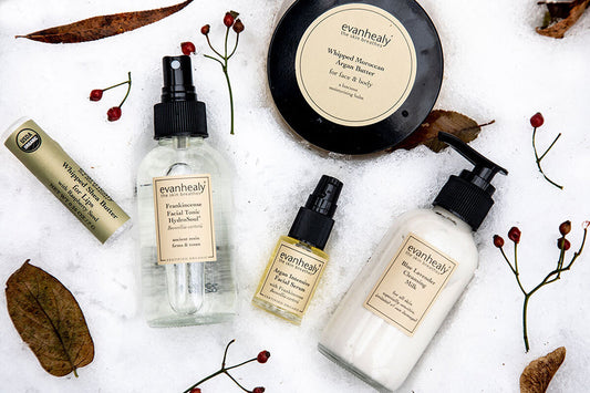 Flat lay of evanhealy skincare products showing jar, pump bottle, spray and oil on snow with dried leaves and berries