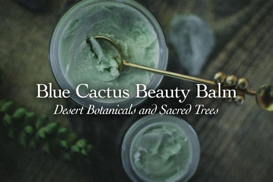 Overhead view of two jars of blue-green beauty balm with a gold spoon on a wooden surface and blurred greenery in the background