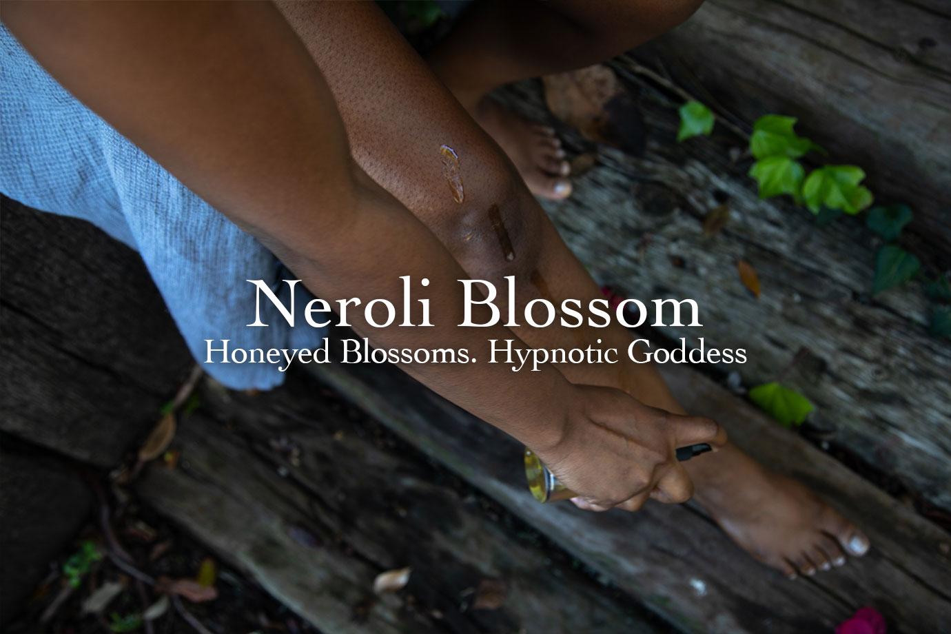 Person applying body oil to their lower legs while seated on a weathered wooden deck, overlaid Neroli Blossom headline