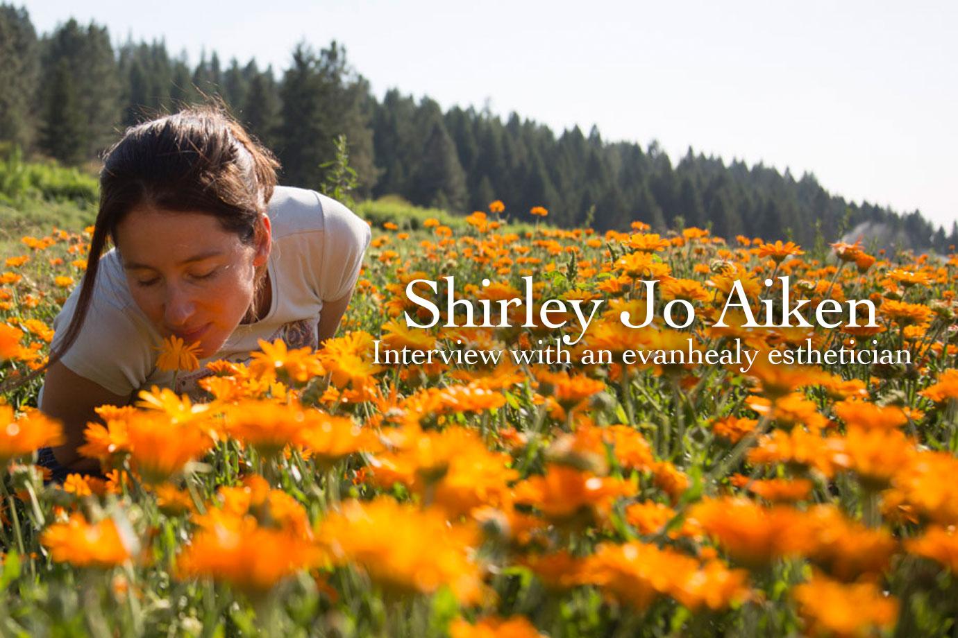 Woman smelling a calendula flower in a field of orange blooms with pine-covered hills in the background