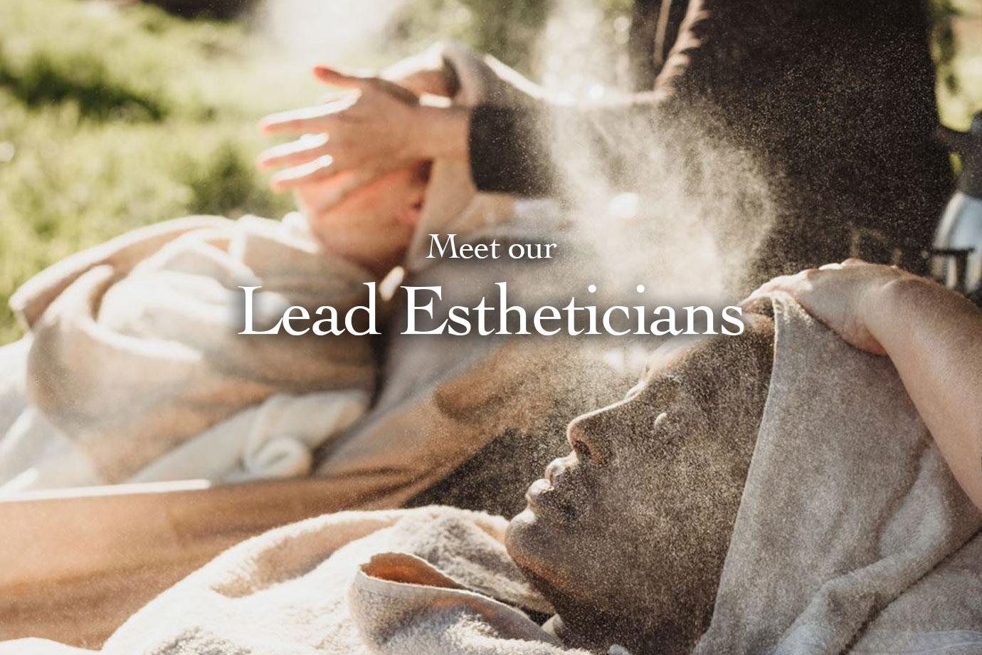 Person reclining with towel over head while an esthetician sprays facial mist outdoors in soft sunlight