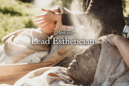 Person reclining with towel over head while an esthetician sprays facial mist outdoors in soft sunlight