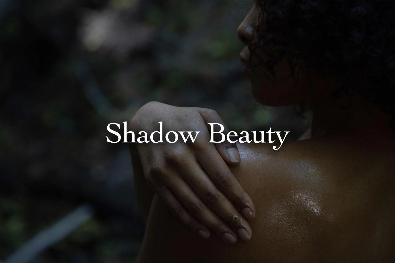Woman resting her hand on her shoulder in low light with overlaid text Shadow Beauty
