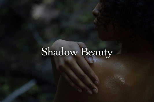 Woman resting her hand on her shoulder in low light with overlaid text Shadow Beauty