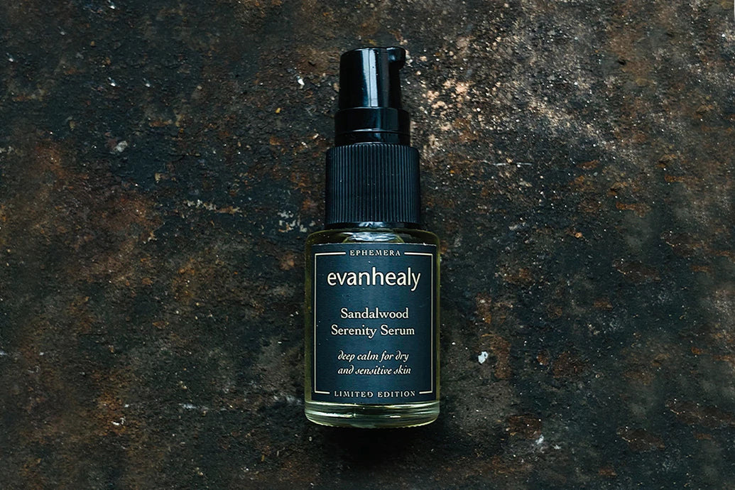 Front view of Sandalwood Serenity Serum bottle showing evanhealy label and black pump on a textured dark metal background