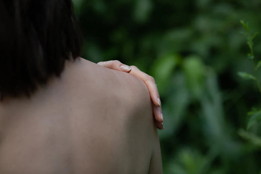 Person’s bare shoulder with hand resting on it against blurred green foliage background