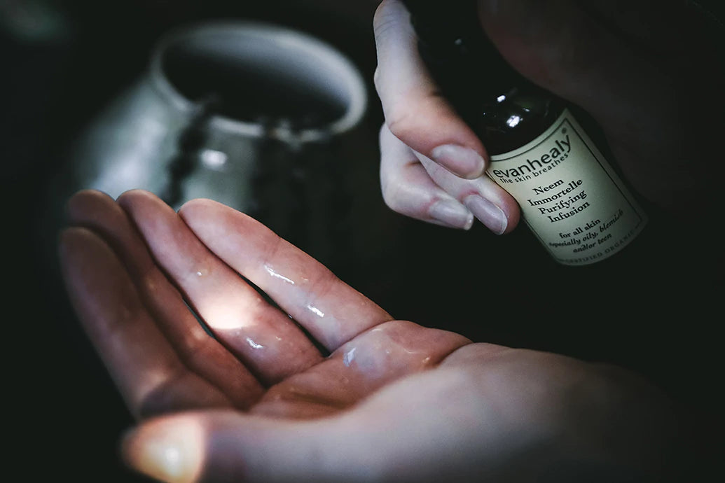 Close-up of hands dispensing evanhealy Neem Immortelle Purifying Infusion serum into palm against a dark background