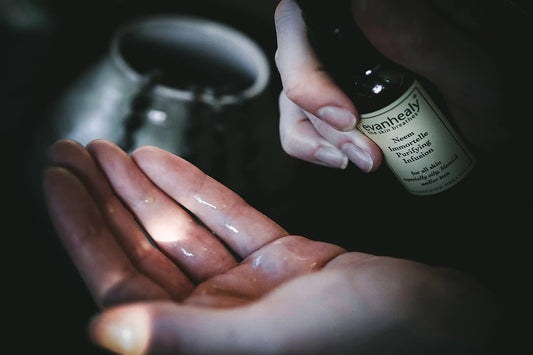 Close-up of hands dispensing evanhealy Neem Immortelle Purifying Infusion serum into palm against a dark background