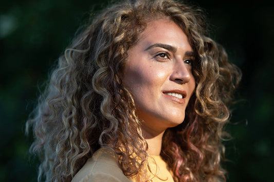 Portrait of a woman with curly hair smiling and looking to the right against a sunlit green background