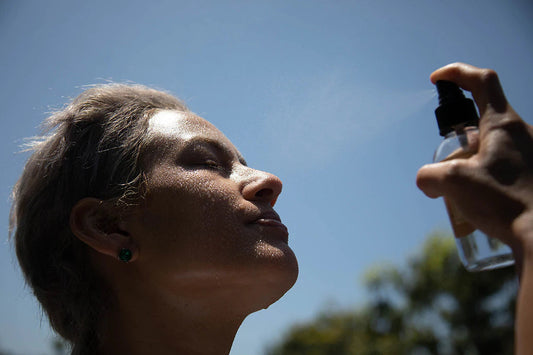 Woman tilting her face up as a spray bottle mists her face outdoors against a clear blue sky