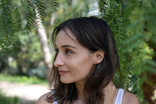 Close-up portrait of a woman looking left among leafy green ferns outdoors