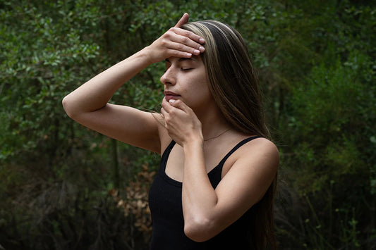Young woman with long hair touching her forehead and chin, eyes closed, in a contemplative pose in a wooded setting