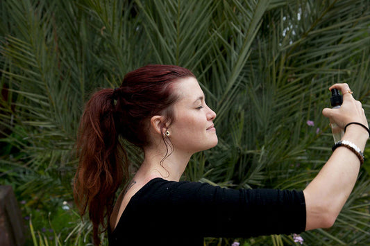 Woman with a ponytail spraying a mist from a spray bottle outdoors in a garden with palm leaves in the background