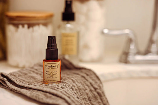 Front view of evanhealy Pomegranate Repair Serum bottle showing pump top and amber glass on a folded gray towel by a bathroom sink