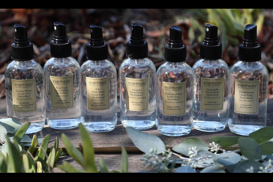 Front view of evanhealy hydrosol spray bottles showing labels and black spray tops on wood with eucalyptus leaves in front