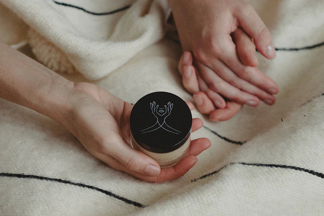 Hands holding a skincare jar on a cozy striped blanket