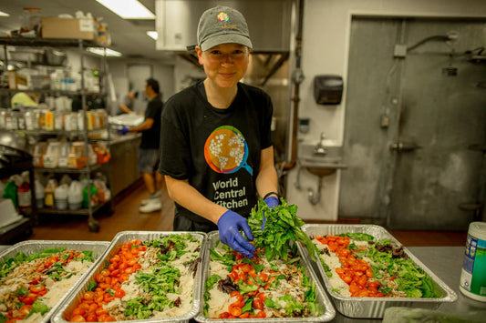 World Central Kitchen volunteer arranging salads in aluminum trays inside a commercial kitchen