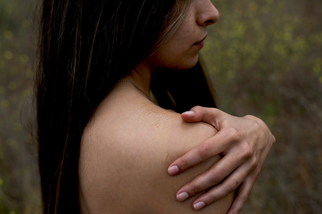 Woman touching her bare shoulder to show moisturized skin in a blurred outdoor field