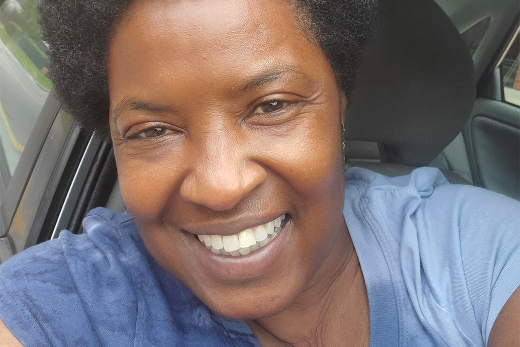 Close-up selfie of a smiling woman wearing a blue shirt inside a car
