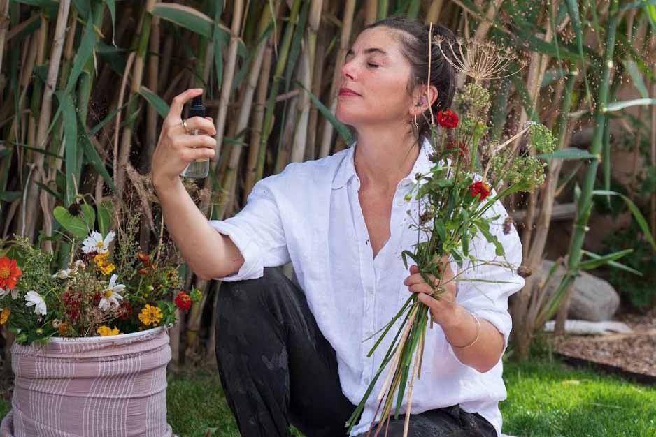 Woman sitting in a garden spraying hydrosol mist onto a bouquet of wildflowers