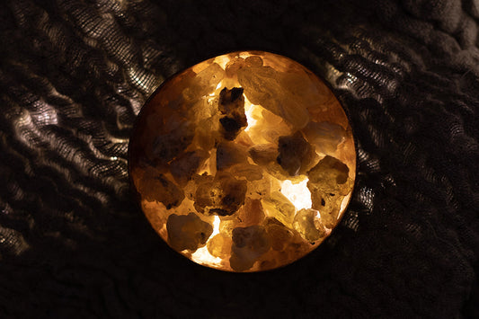 Glowing bowl of frankincense resin lit from within on dark textured fabric