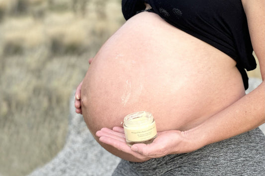 Pregnant woman applying whipped shea butter to her bare belly outdoors