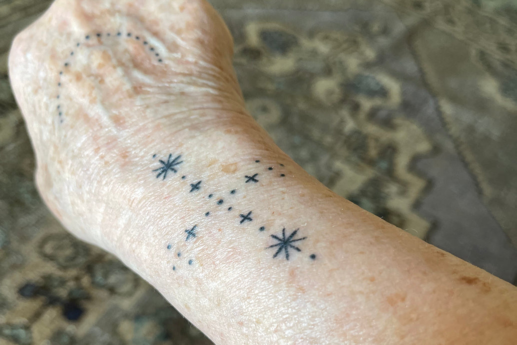 Close-up of a forearm showing a small star-and-dot constellation tattoo with a patterned rug background