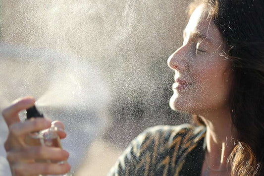 Woman with eyes closed spraying a facial mist with the sunlit fine spray visible