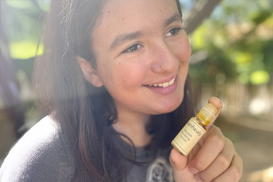 Teen girl smiling outdoors holding a roll-on evanhealy Blemish Purifying Serum near her face