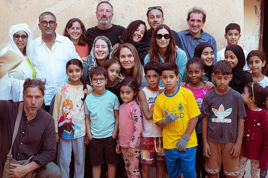 Group of adults and children smiling for a portrait in front of a sunlit plaster wall in Morocco
