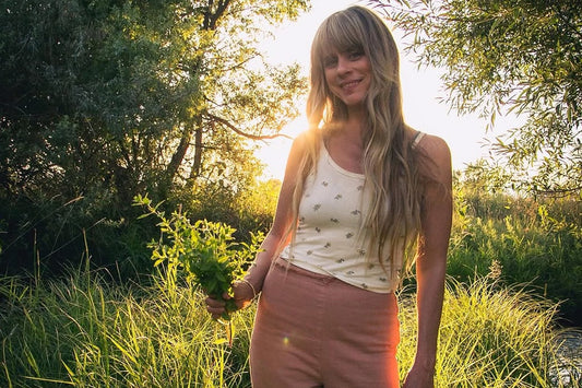 Woman holding a small bunch of fresh herbs in a sunlit grassy meadow at golden hour