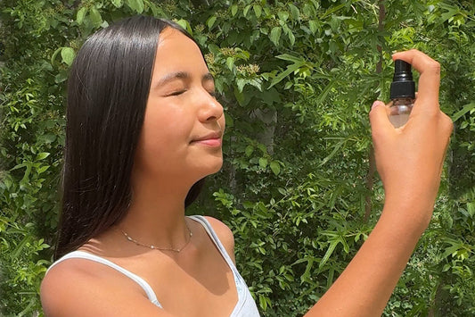 Teen spraying facial mist toward her face in a sunlit garden