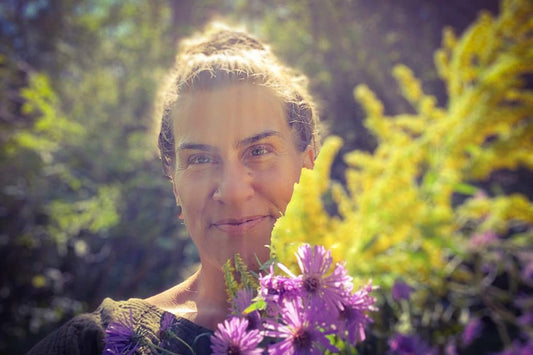 Woman smiling while holding a bouquet of purple asters in a sunlit garden