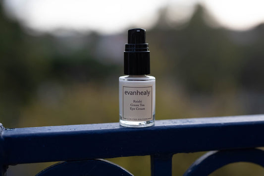 Front view of Reishi Green Tea Eye Cream bottle with black pump and evanhealy label on blue railing, blurred background