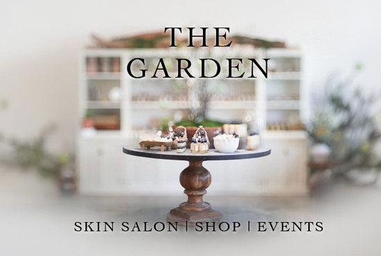 Pedestal table displaying skincare jars in a bright boutique with overlaid text “THE GARDEN” and “SKIN SALON | SHOP | EVENTS”