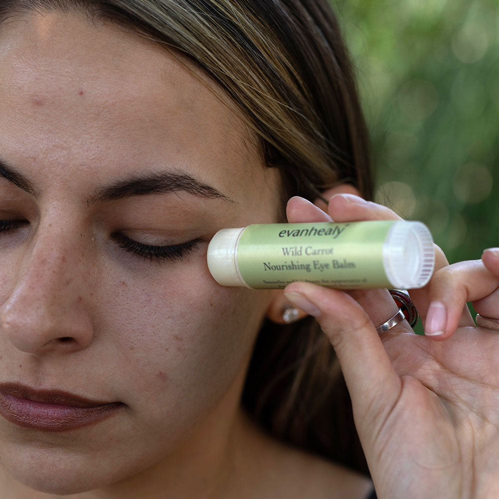 model applying wild carrot immortelle eye balm to alleviate dark circles and puffiness around eyes