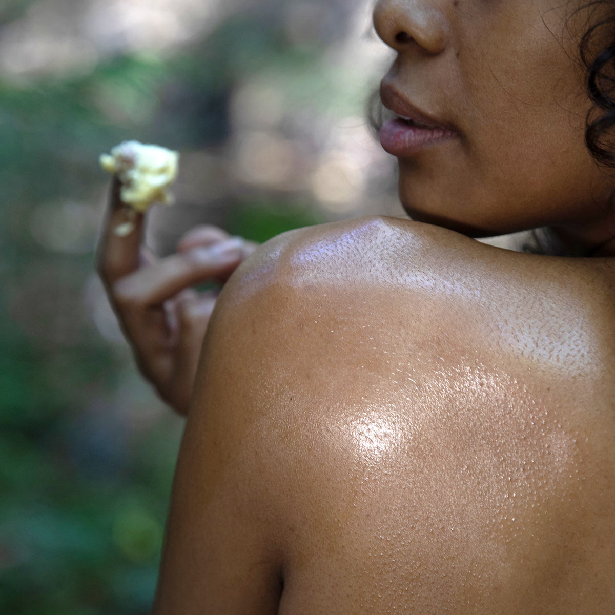 model with clump of shea butter on fingertips and moisture on shoulder