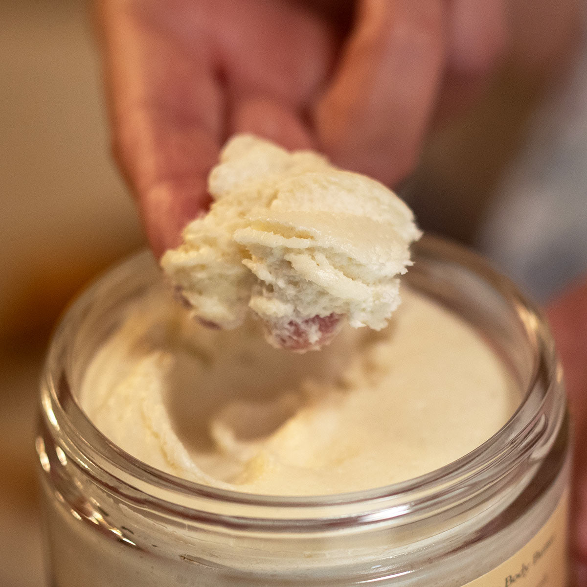 clump of whipped patchouli vanilla body butter on models fingertips