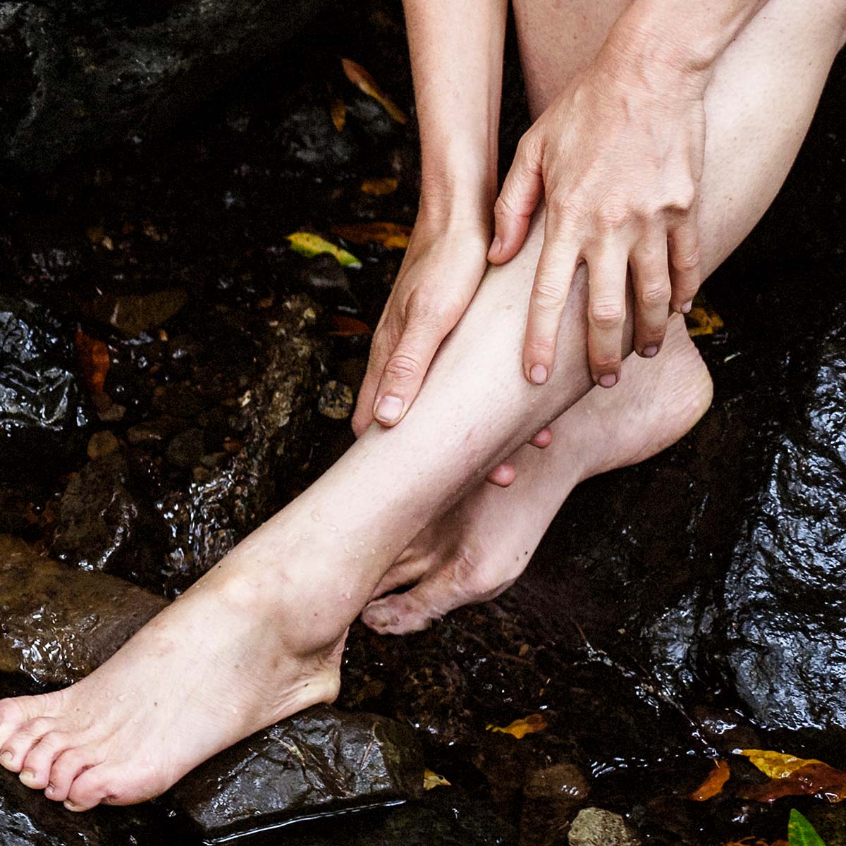 model rubbing body oil on legs in waterfall