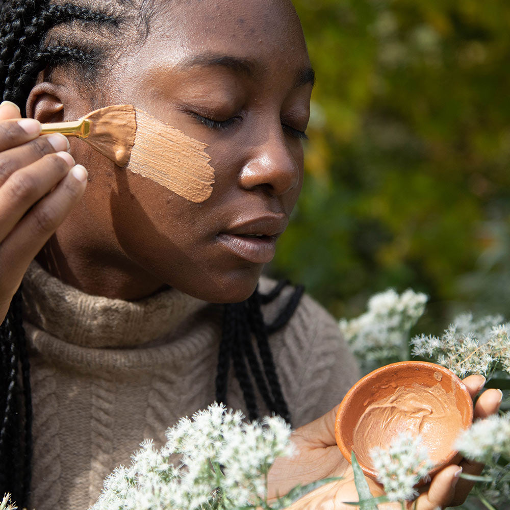model applying french rose clay mask on face outside with fan brush from terra cotta bowl