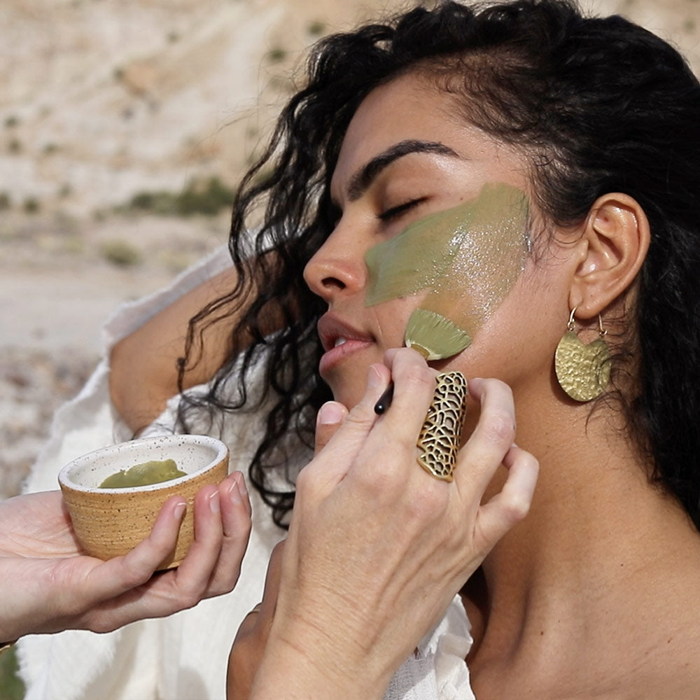 esthetician applying green tea clay mask to models face with boar hair fan brush in santa fe desert